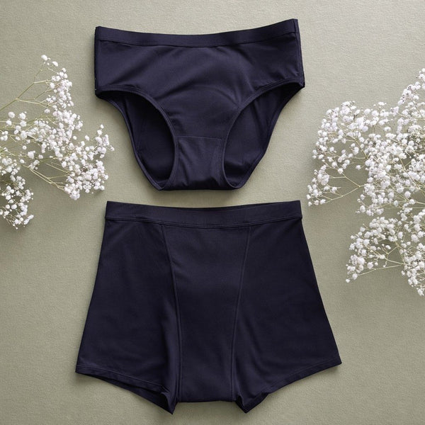 The Her Bloom Keep it Brief, Brief and the Shortie in black, laid flat on a sage background with sprigs of baby's breath