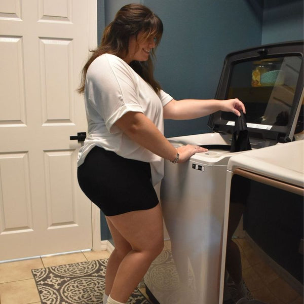 A woman loading a pair of black Her Bloom period underwear into a top-loading washing machine